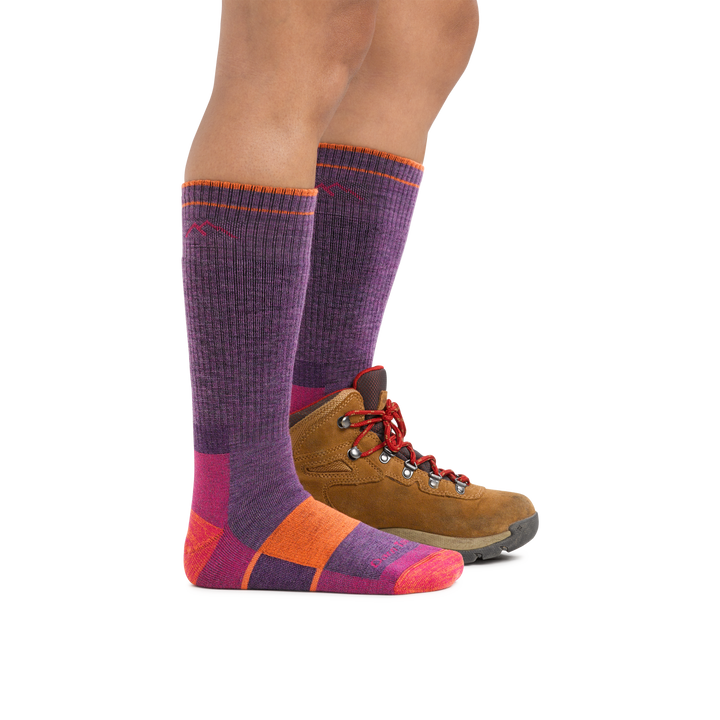 Profile image of a woman's legs on a white background, facing to the right, wearing Women's Hiker Boot Midweight Hiking Socks in Plum Heather with Full Cushion with a hiking boot on one foot