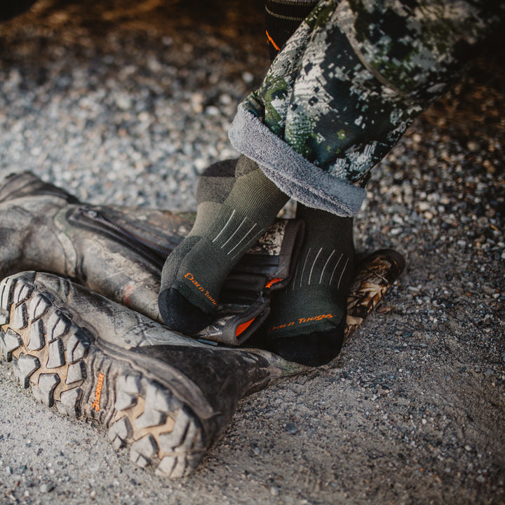 Overhead shot of model in camouflage standing on their boots wearing the men's boot heavyweight hunting sock in forest
