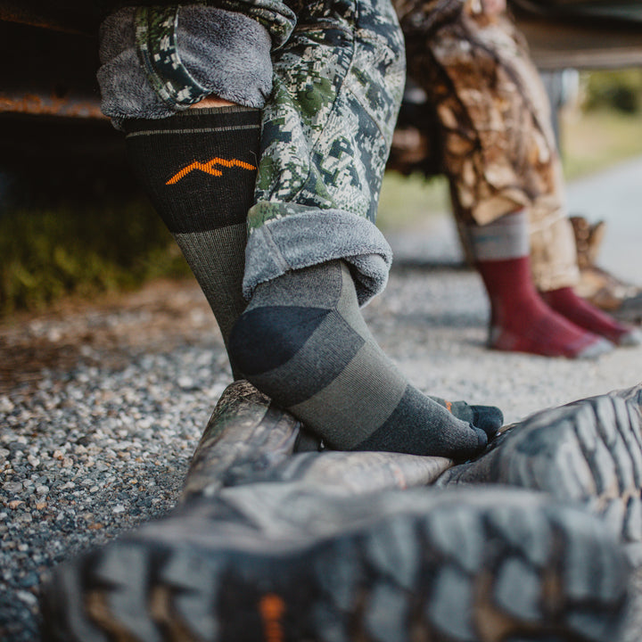 Close up shot of model in camouflage taking off their boots wearing the men's boot heavyweight hunting sock in forest