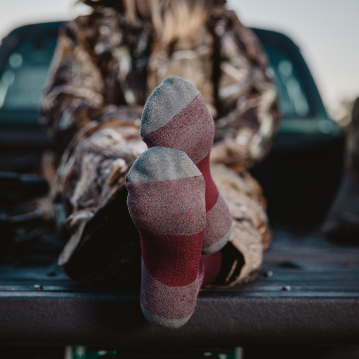 Close up shot of woman sitting in back of pickup truck wearing hunting gear, with feet crossed in the hunter boot socks.