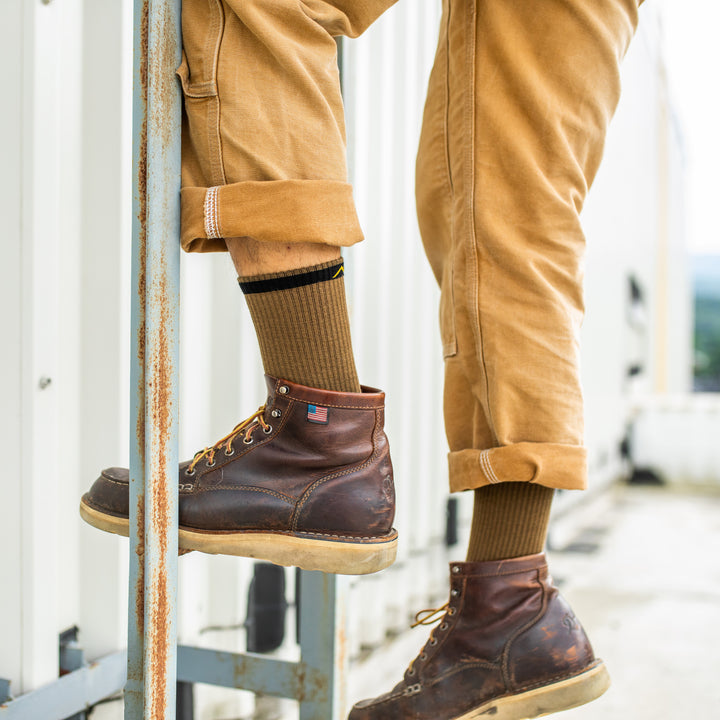 Side shot of model climbing a ladder in work boots wearing the men's fred tuttle micro crew work sock in timber brown