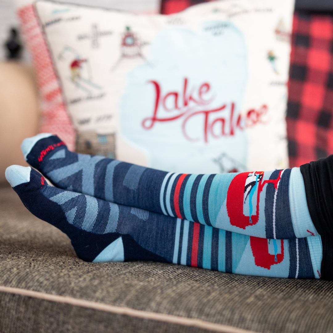 Close up shot of feet crossed on couch wearing the Skipper socks. The socks have a red gondola with a penguin inside.