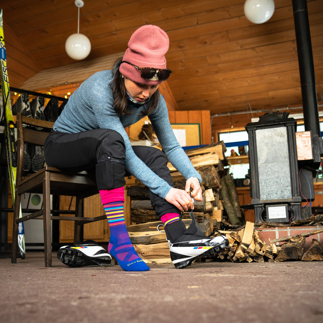 Lifestyle shot of woman putting on nordic ski boots in ski lodge while wearing the Oslo socks.