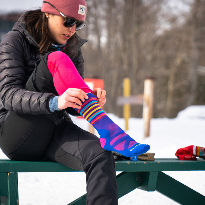 Close up shot of woman putting on Oslo socks on a bench in the snow, getting ready for a nordic ski.