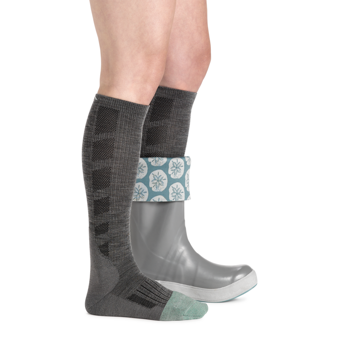 Woman wearing women's emma claire mid-calf work sock in shale gray with gray rubber boot on left foot rolled half down