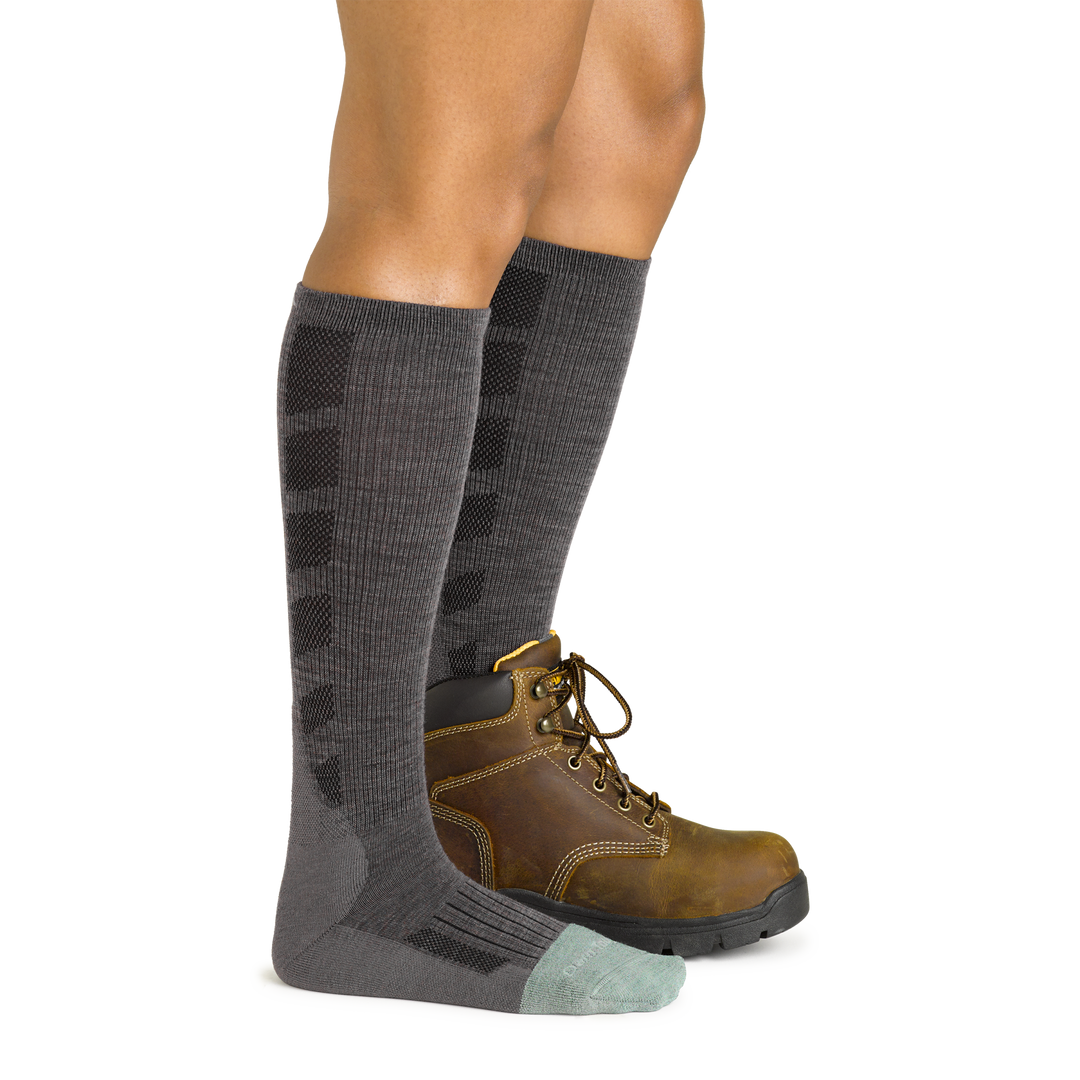 Side studio shot of model wearing women's emma claire mid-calf work sock in shale gray with brown work boot on left foot