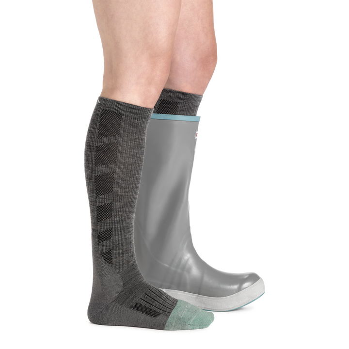 Shot of model wearing women's emma claire mid-calf work sock in shale gray with gray rubber boot on left foot