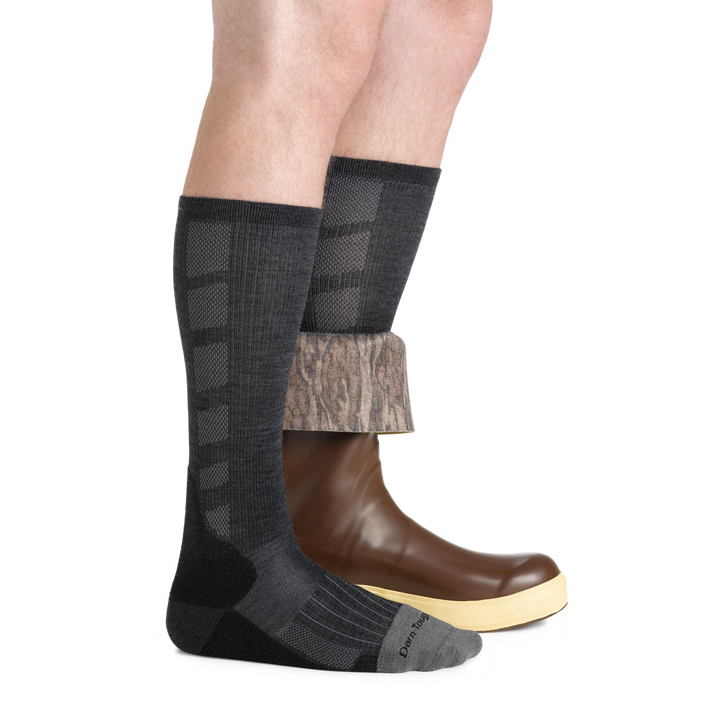 Side studio shot of model wearing men's stanley k mid-calf work sock in gravel gray with rubber boot on left foot folded half down