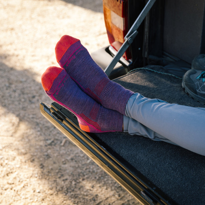 Close up shot of model sitting on tailgate with her feet crossed, wearing hiker quarter socks in Berry and grey leggings.