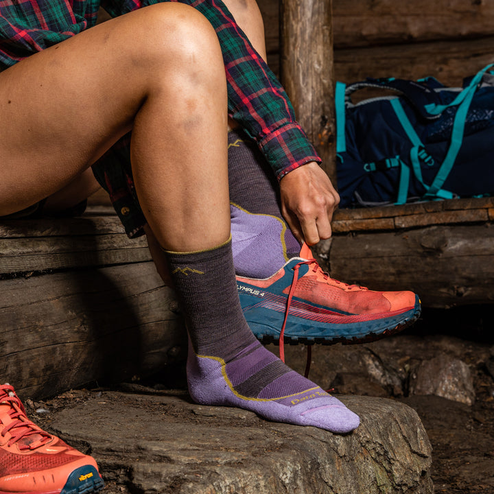 Close up lifestyle shot of model putting on trail runners in her light hikers in Taupe, inside of a lean-to.