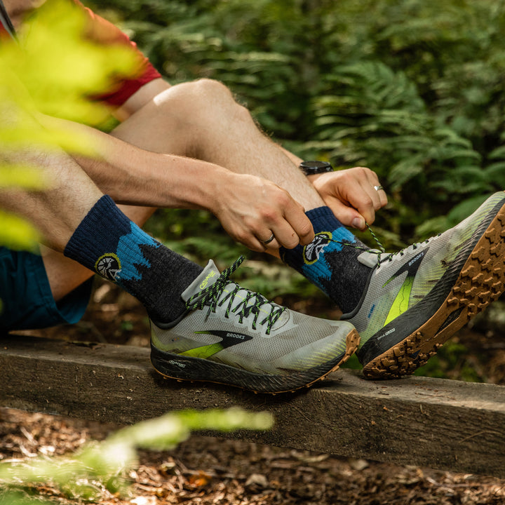 Close up shot of model sitting down in the woods tying their shoe wearing the ATC micro crew hiking sock in eclipse blue