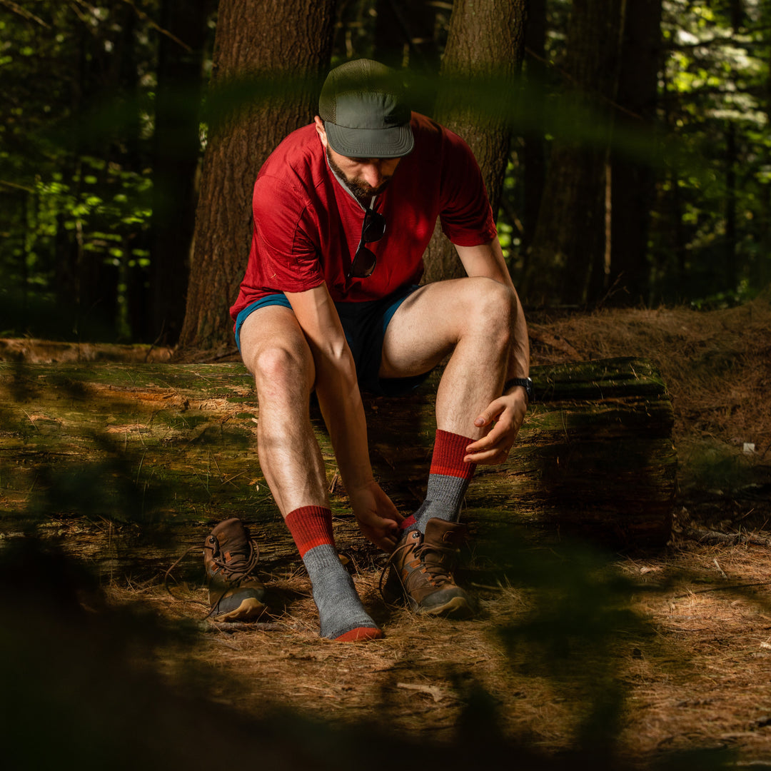 Full shot of model sitting in the woods putting on his shoes while wearing the men's ranger micro crew hiking sock in pepper
