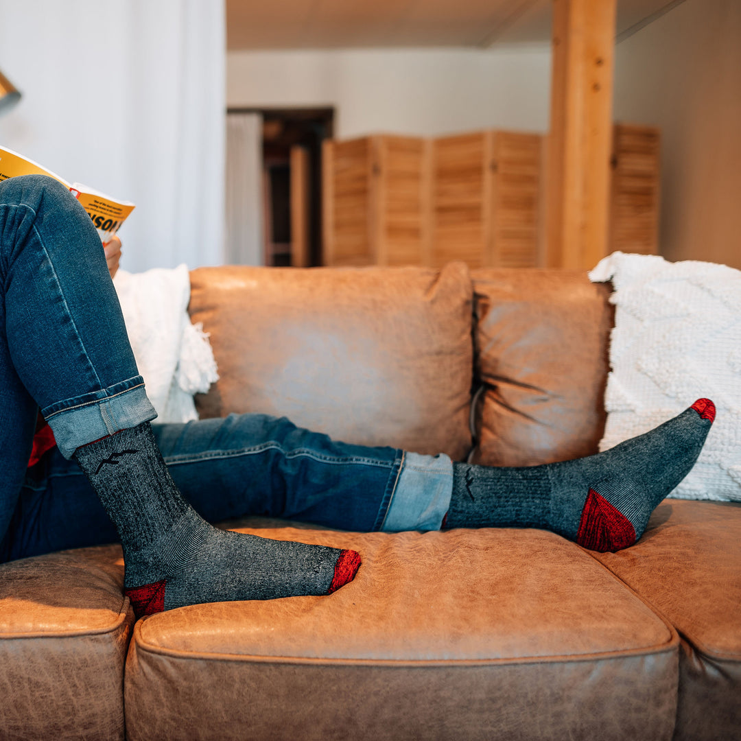 Side shot of model sitting on a leather couch with their feet up wearing the men's mountaineering micro crew hiking sock