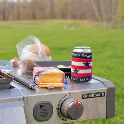 Shelf of a grill with a package of Cheese slices and the Darn Tough Captain Stripe Koozie over a can 