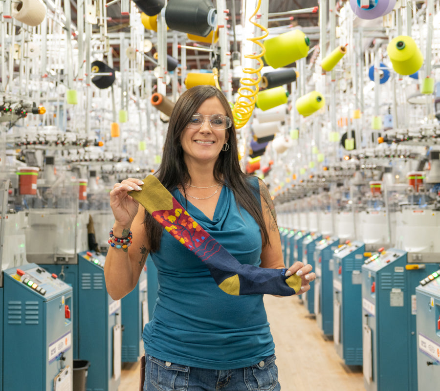 Jessica holding up her favorite sock to gift, the Enchanted ski socks, as she stands inside the Mill