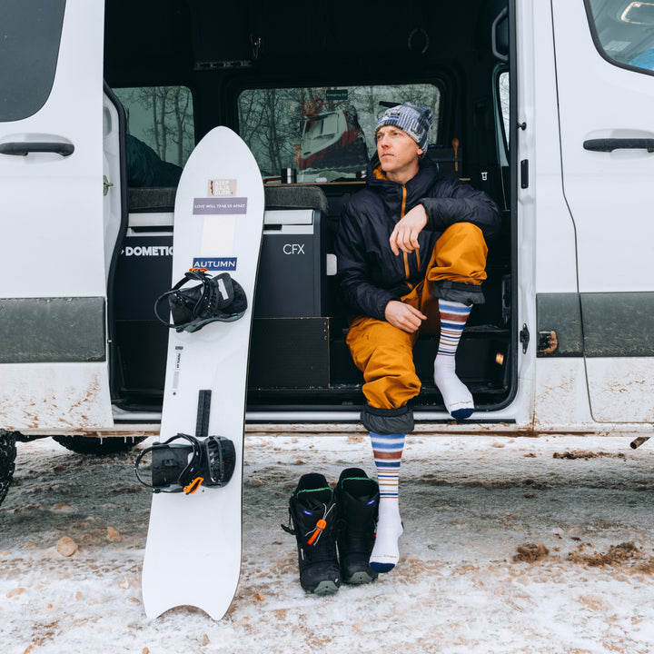 model sitting in van next to snowboard wearing the snowpack in white
