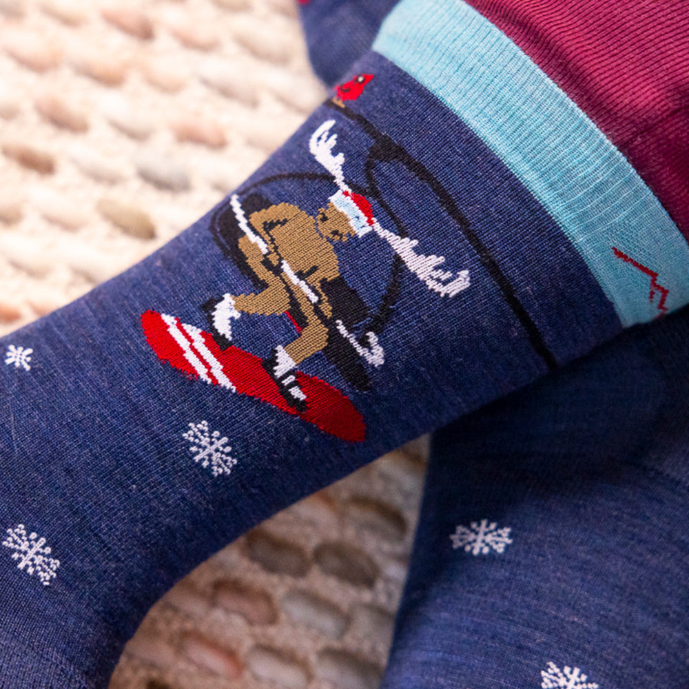 Close-up image of the ankle on the moose on the loose knit to give sock featuring the moose on the ski lift with snowboard