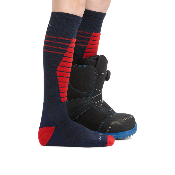 Kid wearing Edge Over the Calf Midweight Ski & Snowboard socks in Eclipse, with a snowboard boot on the back foot