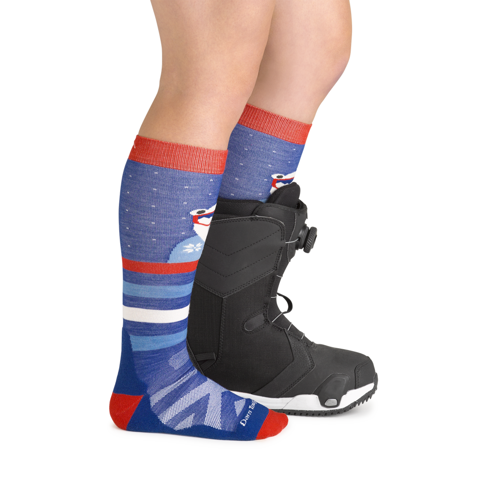 Model wearing kid's polar patroller over-the-calf ski sock in blue with black snowboard boot on left foot