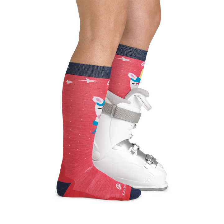 Model wearing kid's magic mountain over-the-calf ski sock in raspberry with white snowboard boot on left foot