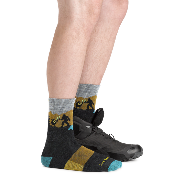  Side shot of model wearing the men's close encounters micro crew hiking sock in Charcoal with a hiking shoe on his left foot