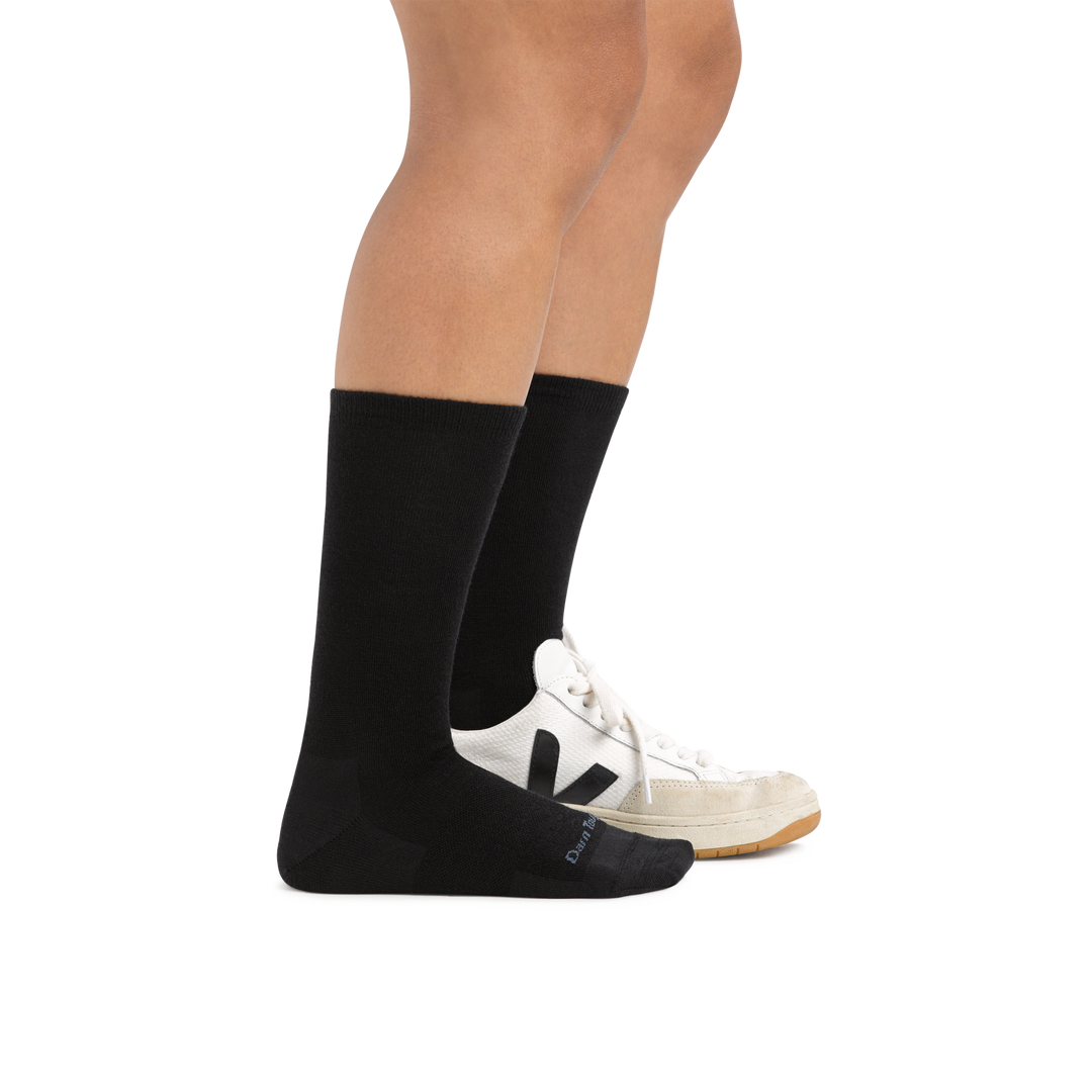 Woman wearing Women's Solid Basic Crew Lightweight Lifestyle Sock in Black with one foot also in a casual shoe
