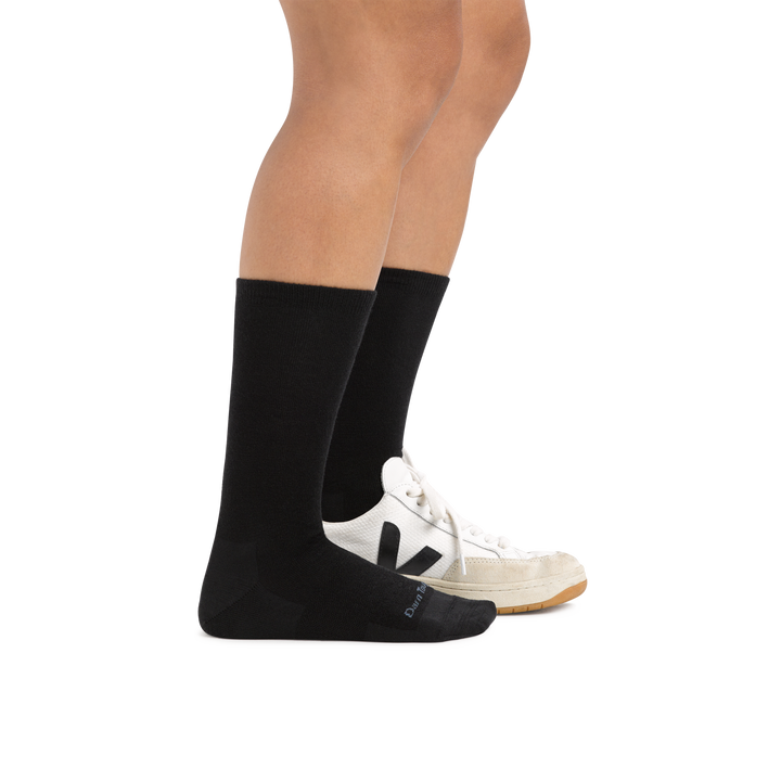 Woman wearing Women's Solid Basic Crew Lightweight Lifestyle Sock in Black with one foot also in a casual shoe