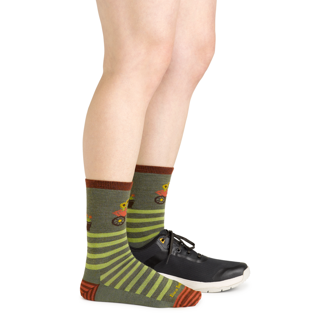 Side studio shot of model wearing women's animal haus crew lifestyle sock in herb green with black sneaker on left foot