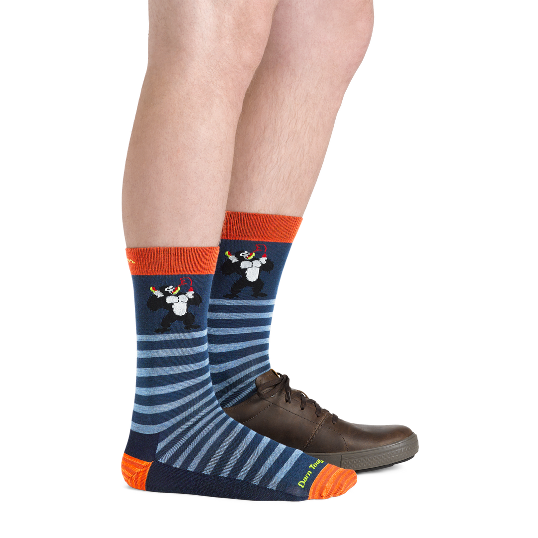Side shot of model wearing the men's animal haus crew lifestyle sock in deep water colorway with a brown shoe on his left foot