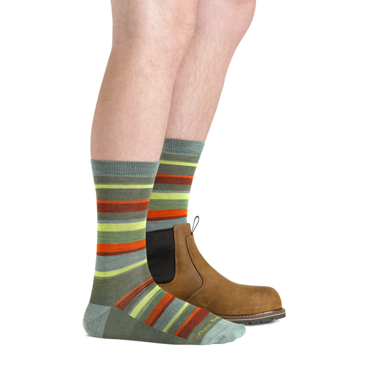 Side studio shot of model wearing men's druid crew lifestyle sock in cedar with brown boot on left foot