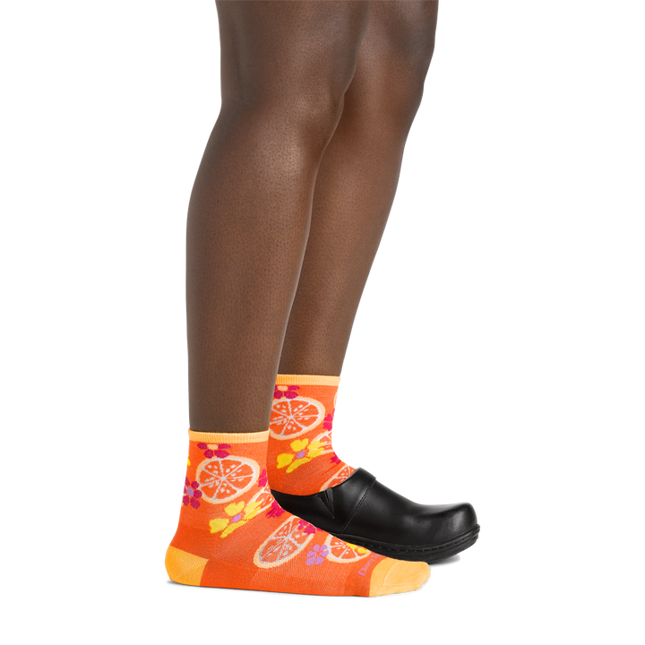  Model wearing the women's fruit stand shorty lifestyle socks in grapefruit colorway with a black clog on her left foot