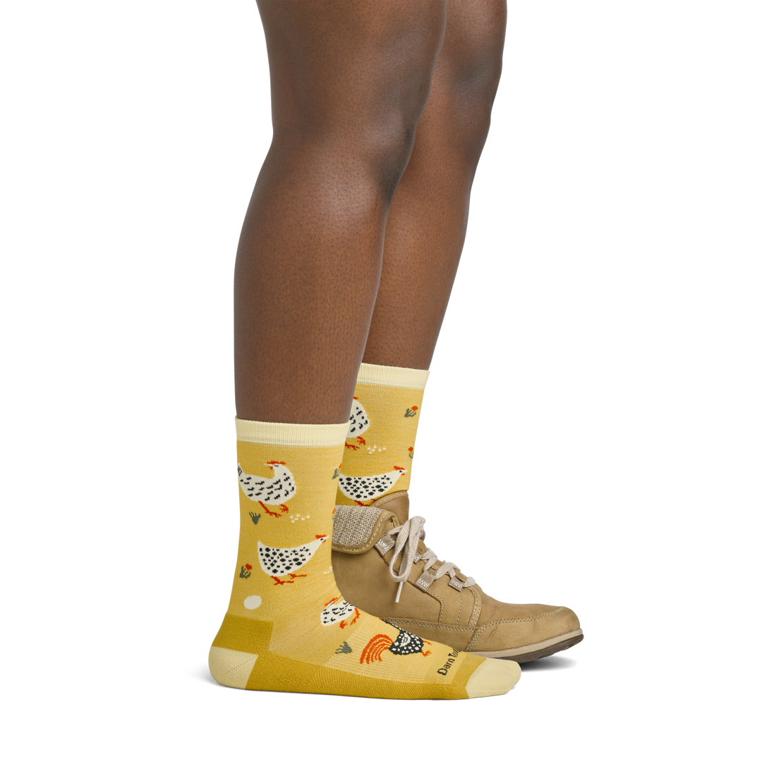 Image of model wearing 6114 Mother Clucker socks in Sunny colorway anda brown hiking boot on one foot