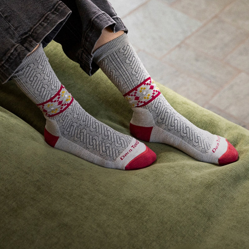 Feet wearing gray cable knit socks with a red and gold nordic pattern
