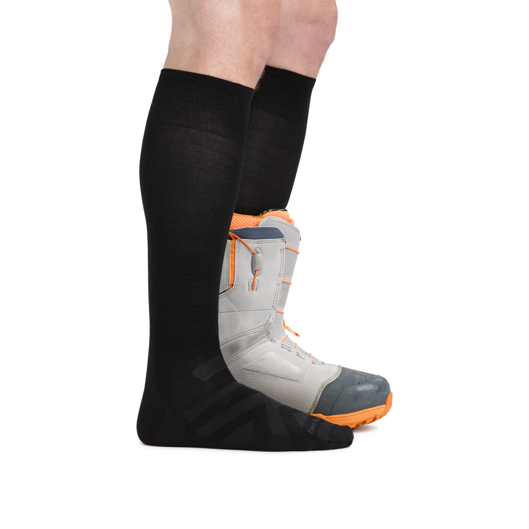 Man wearing RFL Over the Calf Ultralightweight Ski & Snowboard Sock in Black,  with back foot wearing a snowboard boot