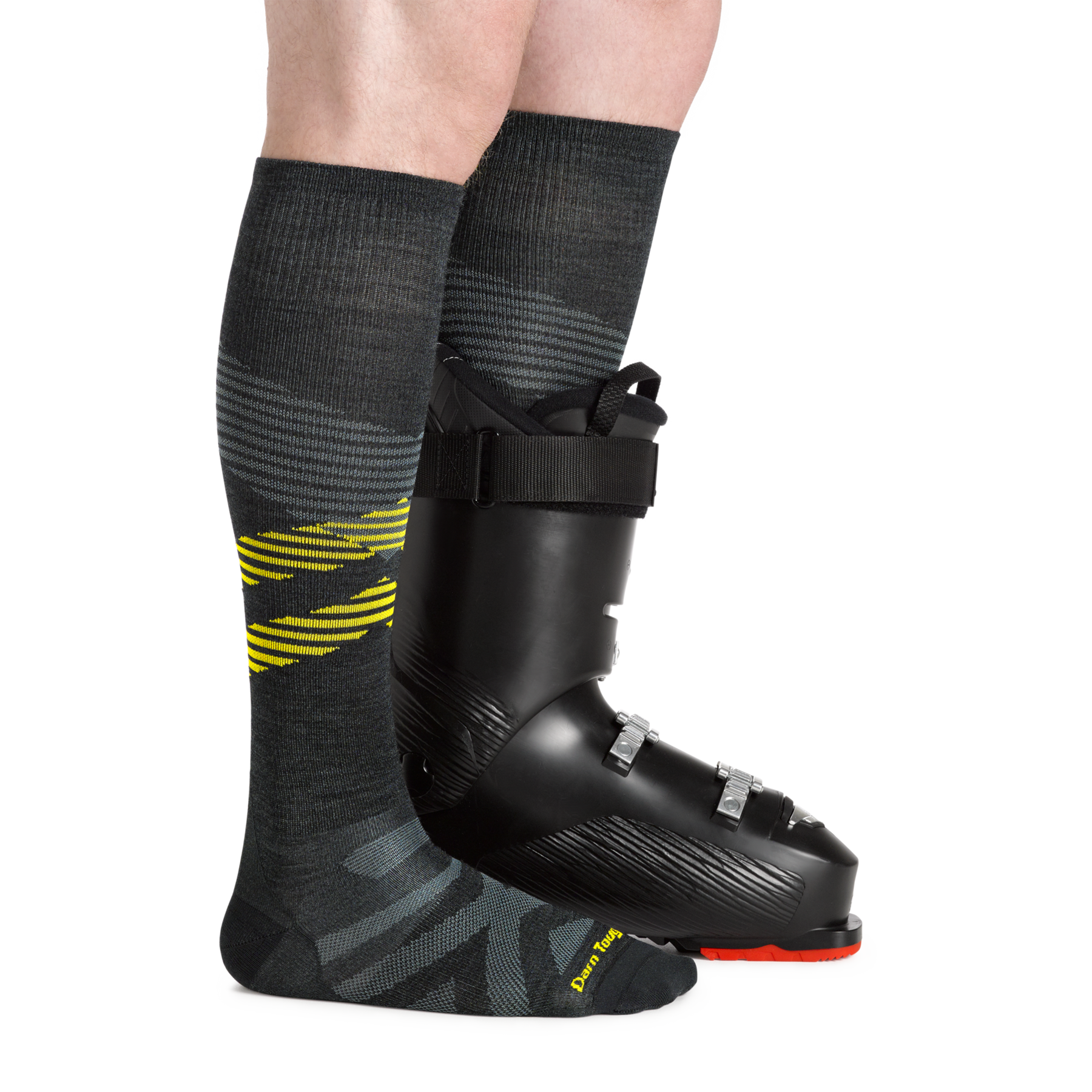 Side studio shot of model wearing men's pennant RFL over-the-calf snow sock in carbon with black snow boot on left foot