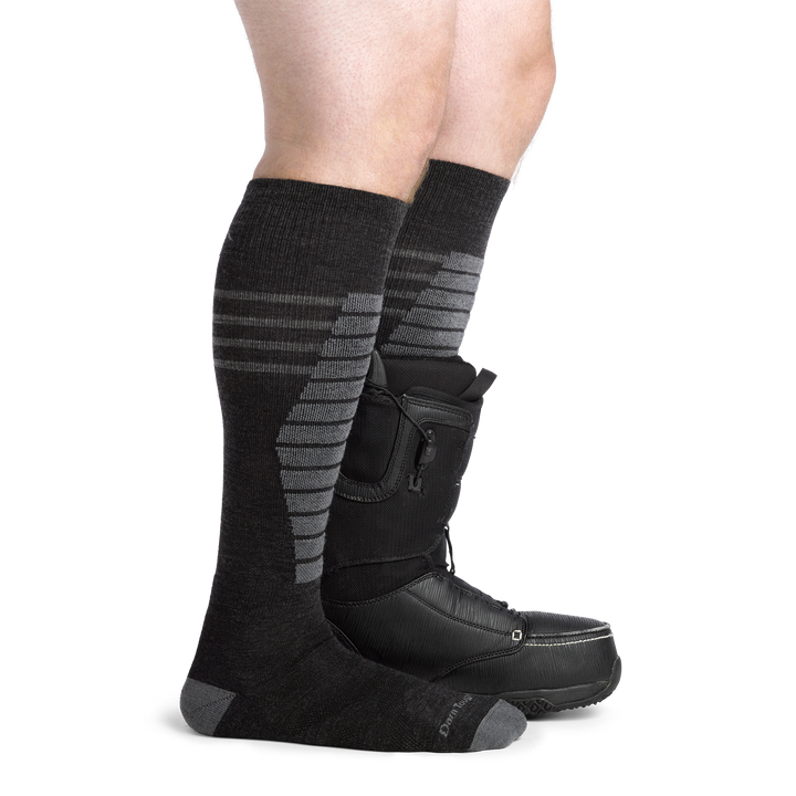 Model wearing men's edge over-the-calf midweight snow sock in Charcoal with black ski boot on left foot