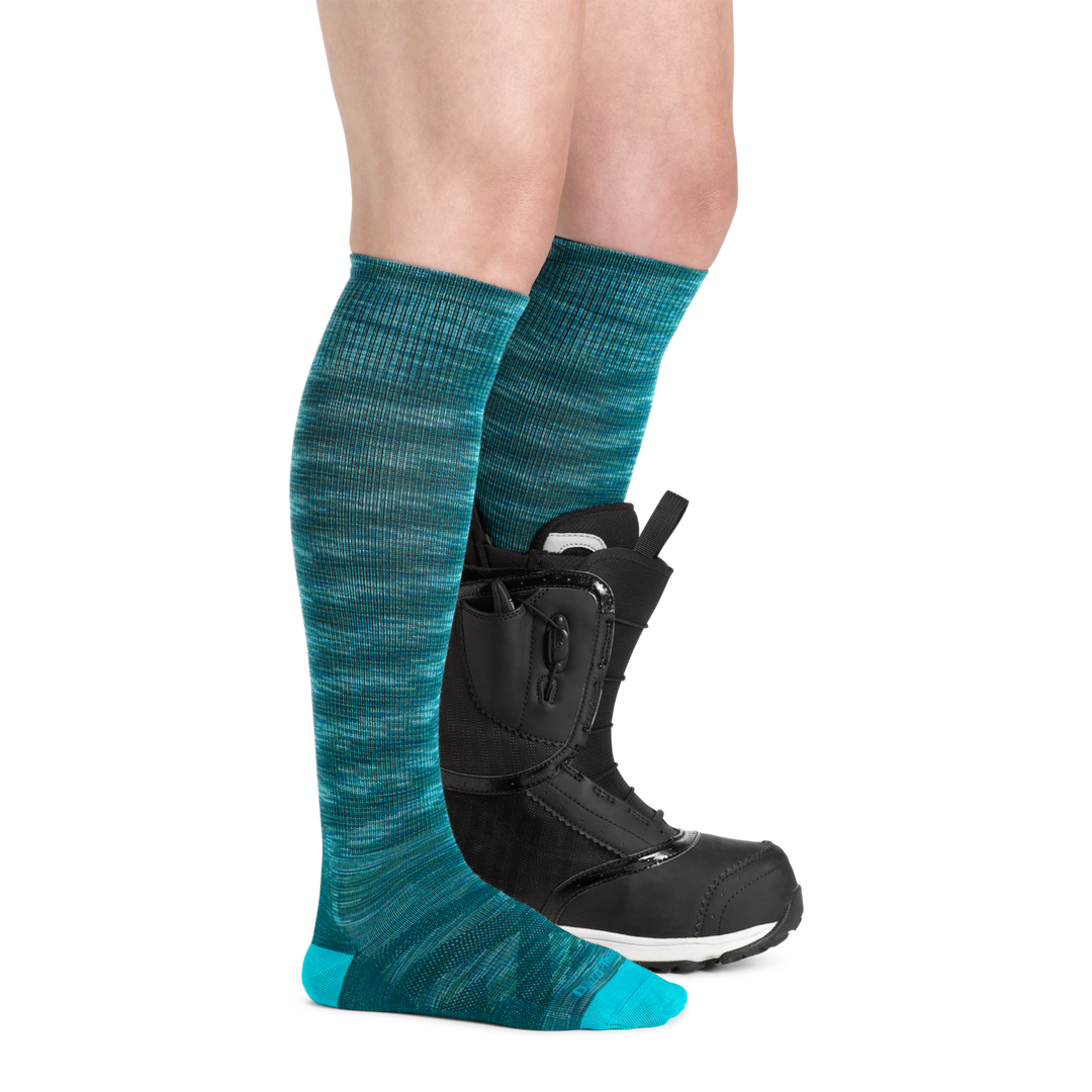 Profile image of a woman's legs, wearing Women's RFL Over the Calf Ultra-Lightweight Ski & Snowboard Socks in Neptune with one foot also in a ski boot