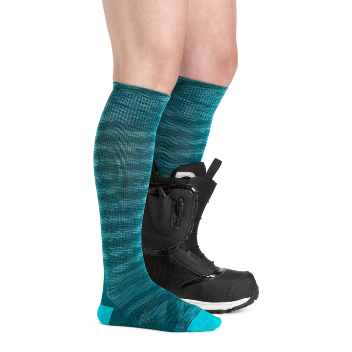 Profile image of a woman's legs, wearing Women's RFL Over the Calf Ultra-Lightweight Ski & Snowboard Socks in Neptune with one foot also in a ski boot