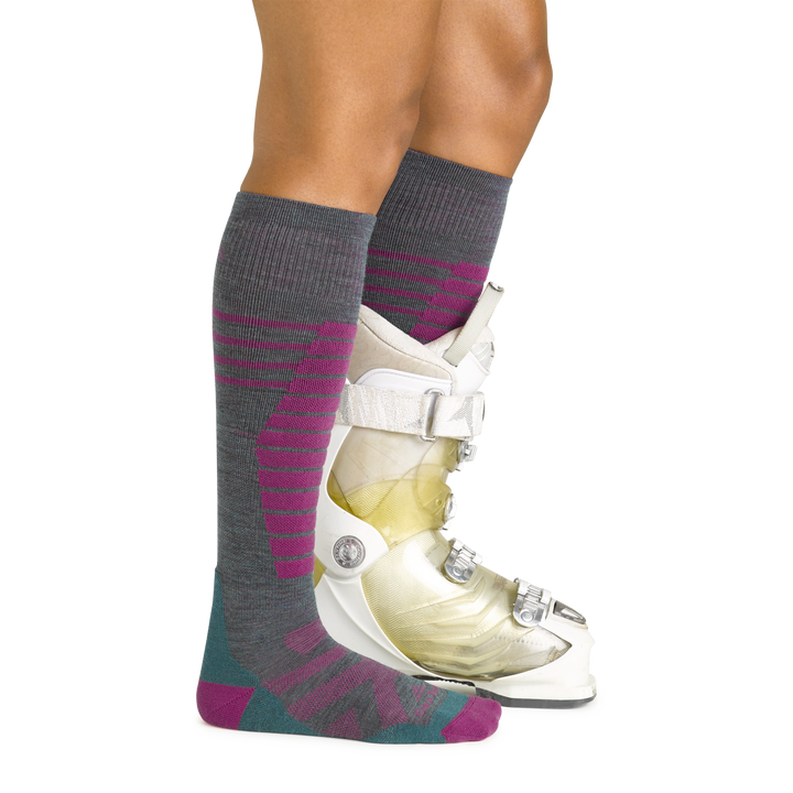 Side studio shot of model wearing women's edge over-the-calf snow sock in teal with white ski boot on left foot