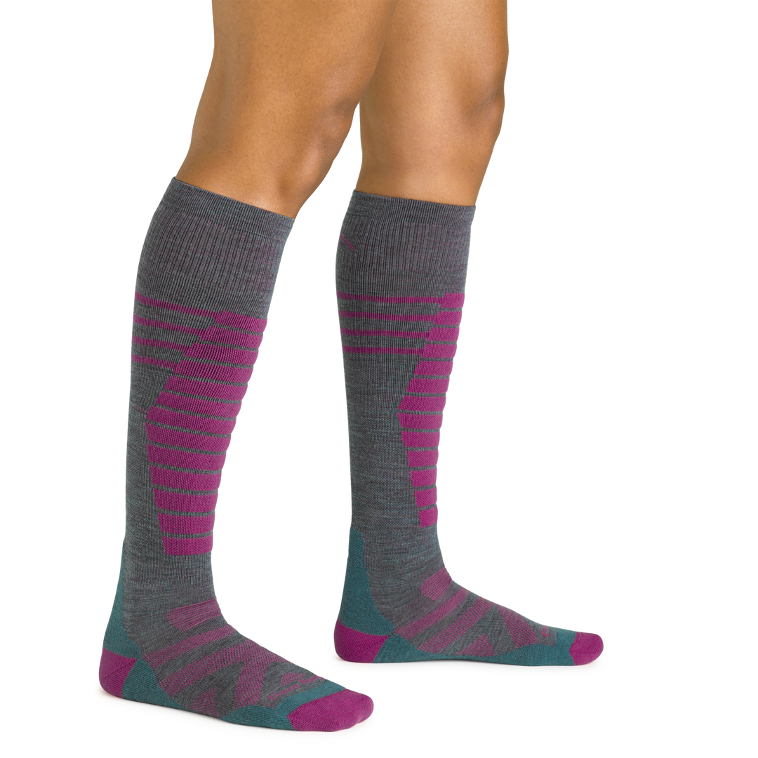 Close up studio shot of model wearing women's edge over-the-calf midweight ski & snowboard sock in teal and pink