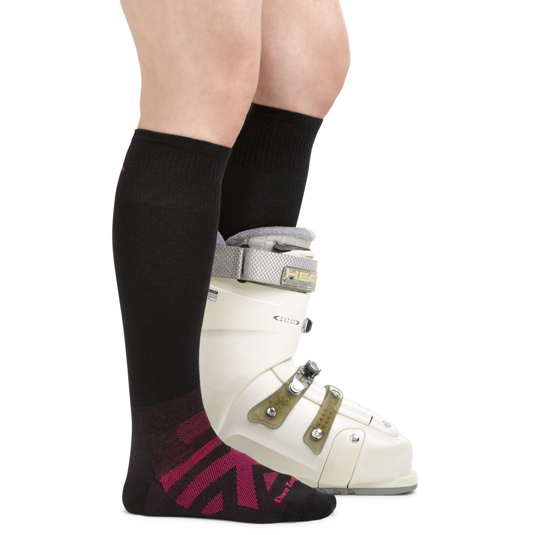 Side shot of model wearing RFL over-the-calf ski & snowboard sock in black with a white ski boot on one foot