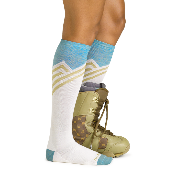 Model wearing women's peaks ove-the-calf lightweight snow sock in white with green snow boot on left foot