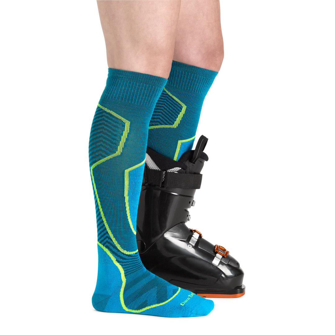 Profile image of a woman's legs, facing to the right, wearing Women's Outer Limits Over the Calf Midweight Ski and Snowboard Socks in Cascade and a ski boot on one foot