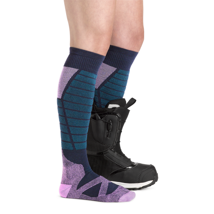Profile image of a woman's legs facing to the right, wearing Women's Function X Over the Calf Midweight Ski and Snowboard Socks in Eclipse and a ski boot on one foot