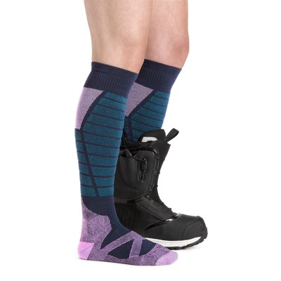 Profile image of a woman's legs facing to the right, wearing Women's Function X Over the Calf Midweight Ski and Snowboard Socks in Eclipse and a ski boot on one foot