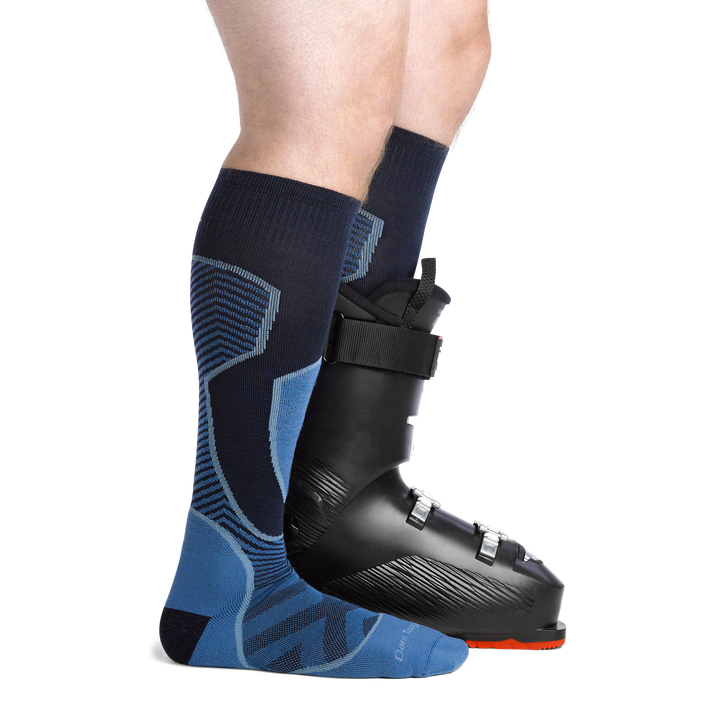 Man facing to the right, wearing Outer Limits Over the Calf Ski & Snowboard Socks in Cobalt, back foot also wearing a Ski boot