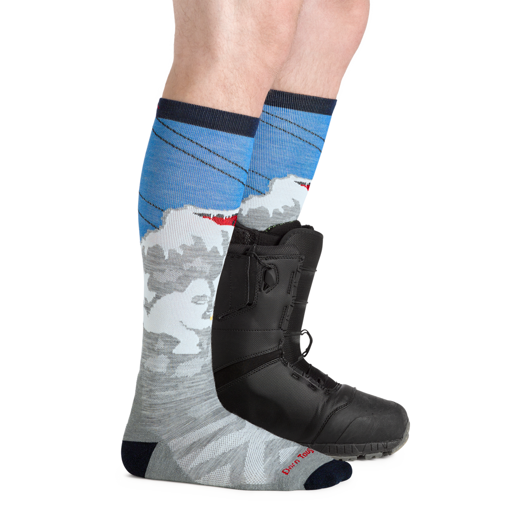 Man facing to the right, wearing Heady Yeti Over the Calf Ski & Snowboard Socks in Gray, back foot also wearing a snowboard boot