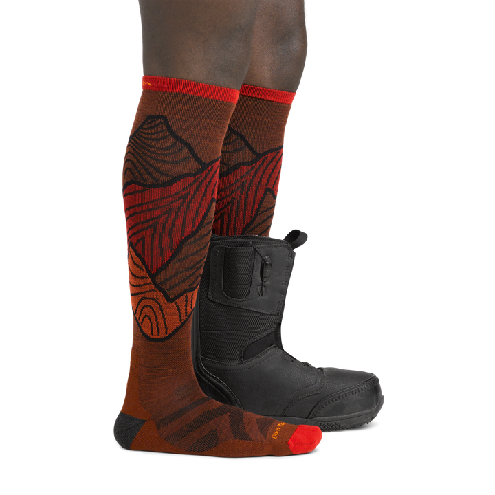 Image of model wearing 5050 Titan socks in Fireball colorway on one foot and snowboard boot on the other