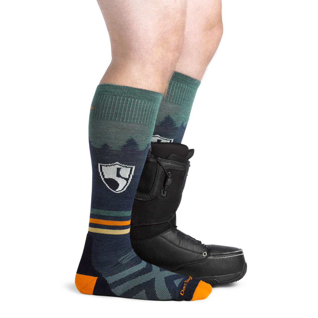 Man facing to the right, wearing High Fives Ski and Snowboard Socks in Eclipse, back foot wearing a Snowboard boot