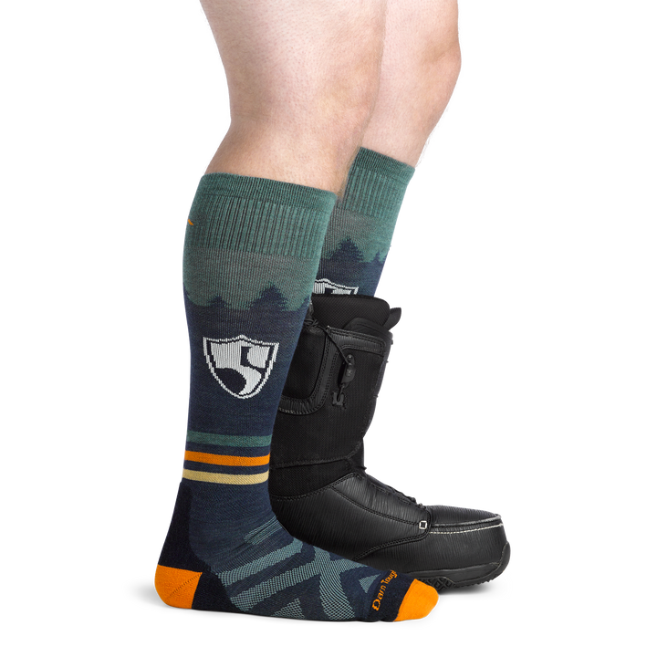 Man facing to the right, wearing High Fives Ski and Snowboard Socks in Eclipse, back foot wearing a Snowboard boot